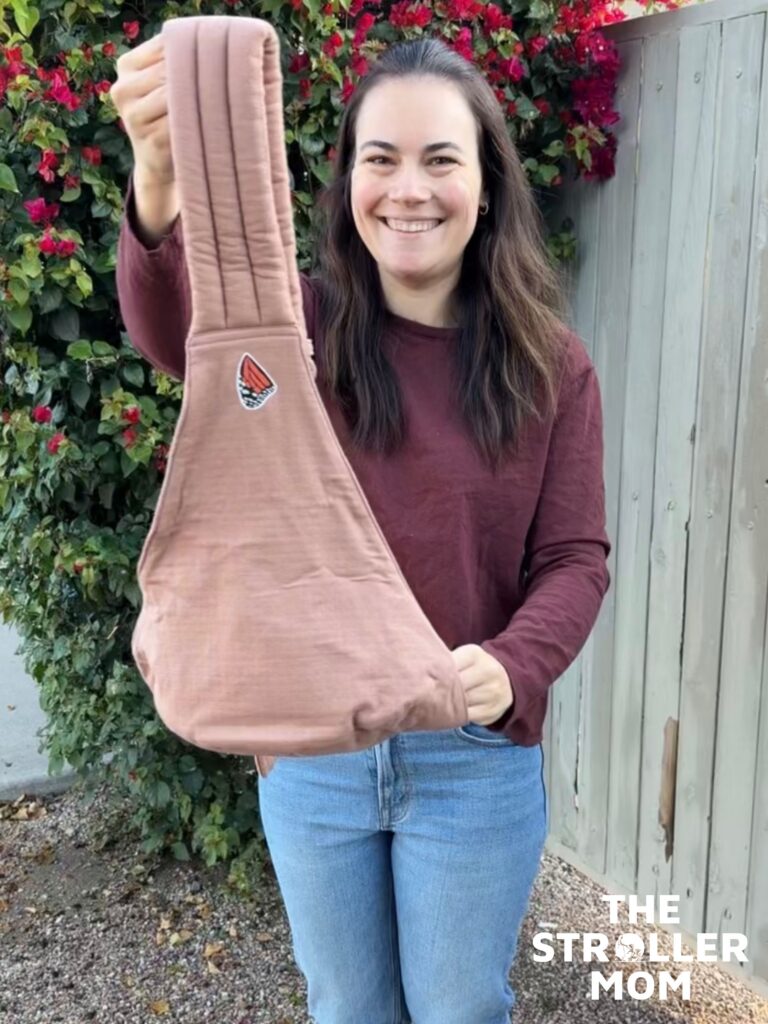 Emily from The Stroller Mom holding up the Mabe Monarch Toddler Sling in Mocha to show the padded shoulder strap and seat