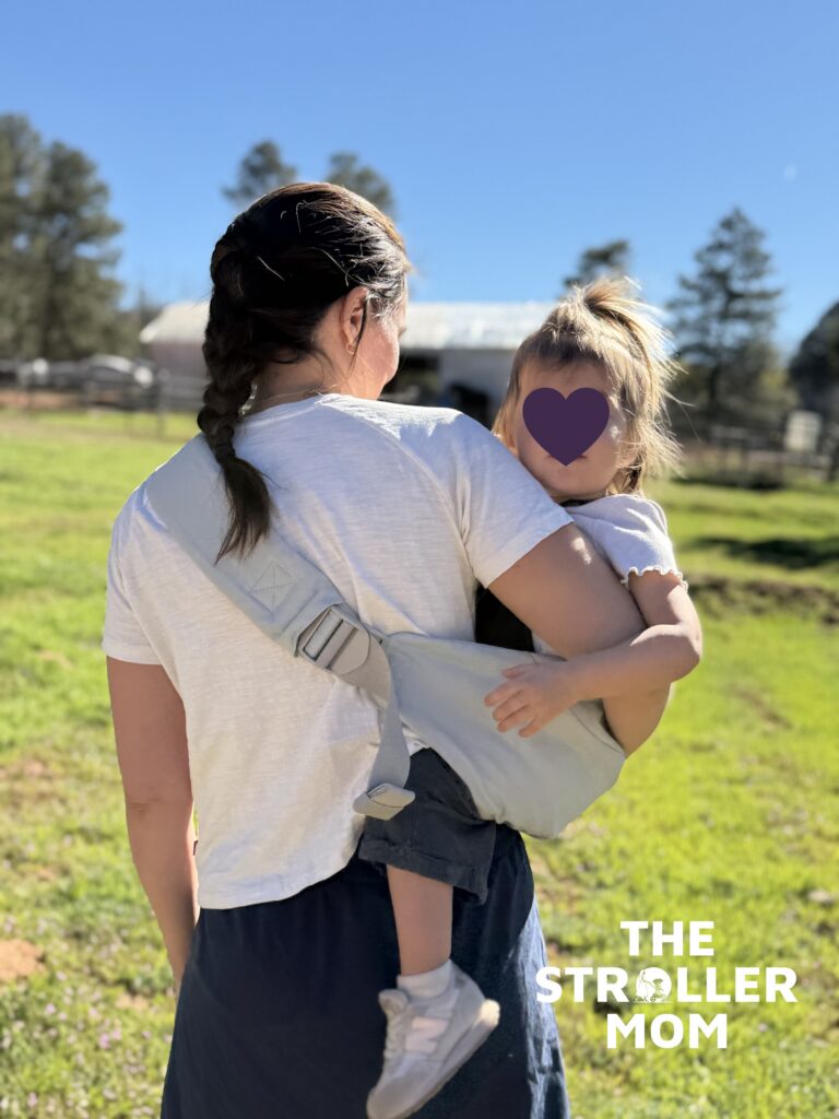 Back view of parent carrying a 2 year old in the Ergobaby Upsie Sling showing shoulder strap fit
