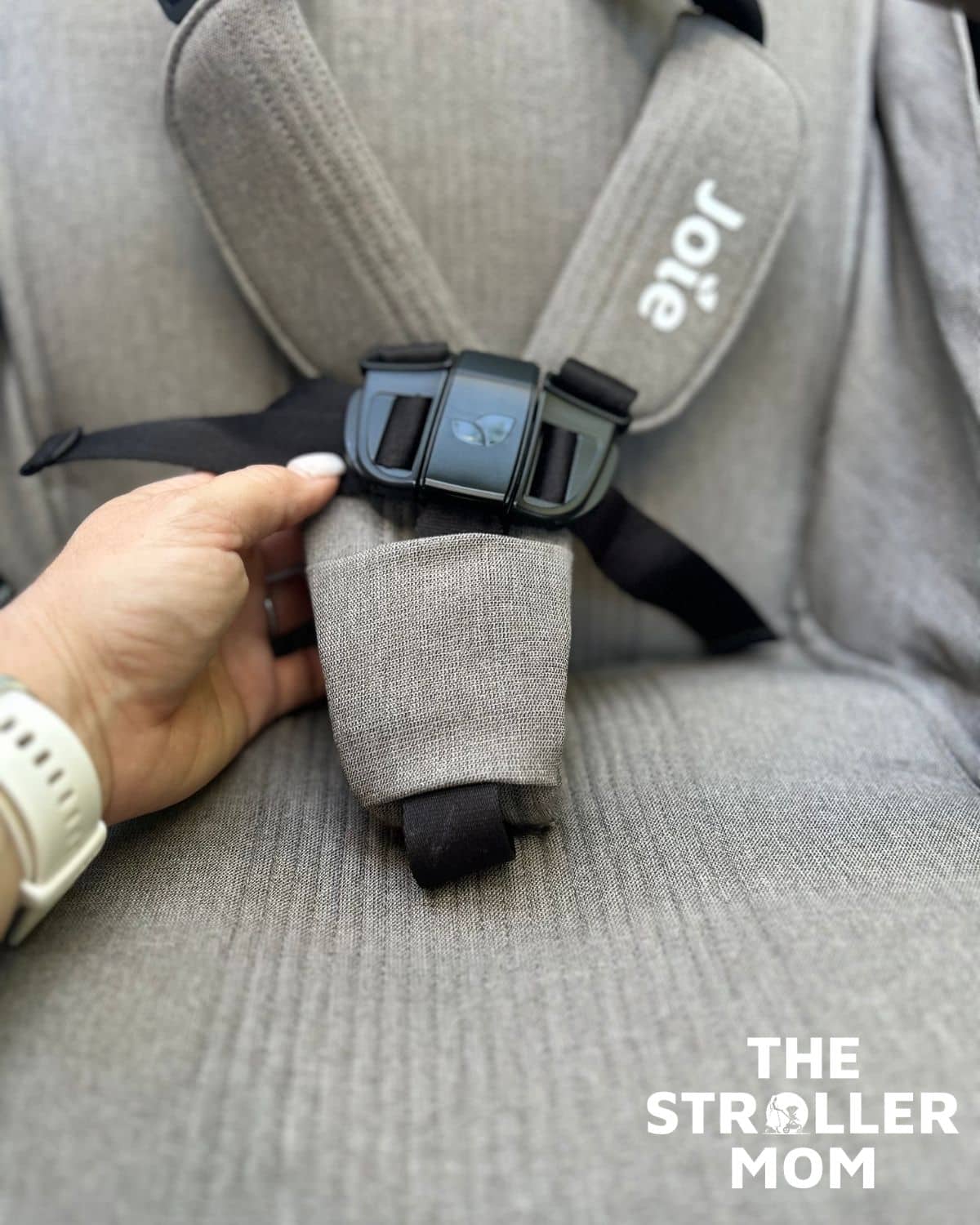 Hand holding the Joie Nutmeg harness buckle and shoulder pads