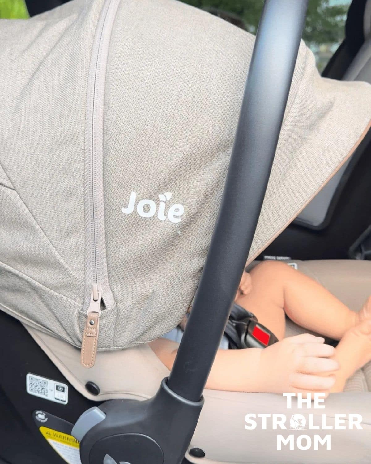 Joie Mint Latch infant car seat installed in the back seat with the canopy covering the child's face