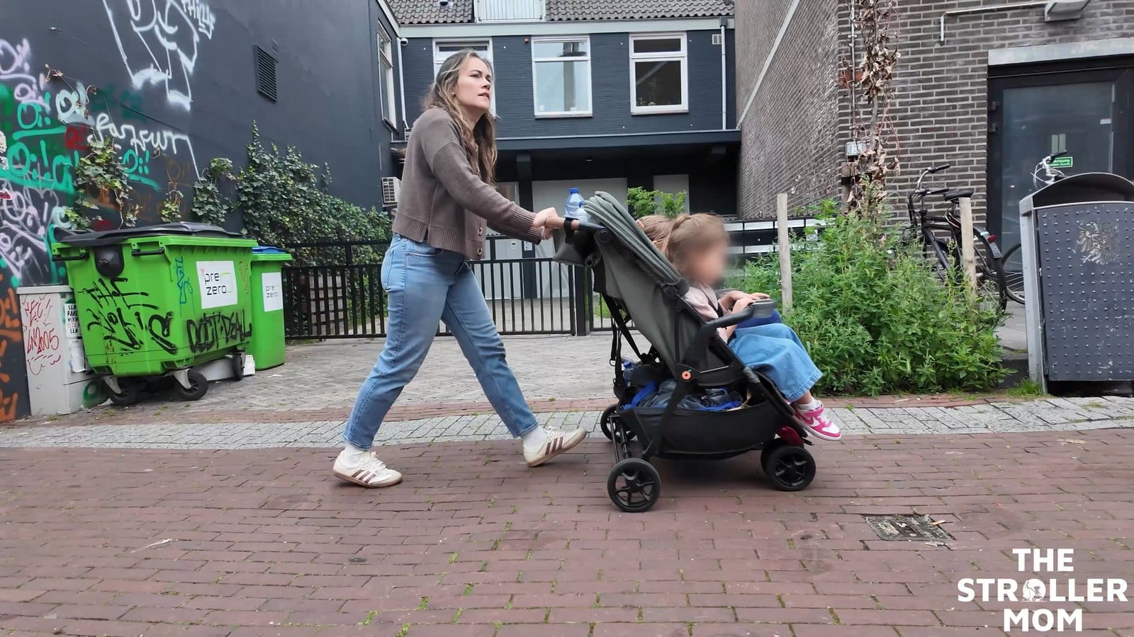 Side view of Emily pushing the Zoe Twin V3, showing the handlebar, walking stride and loaded basket.