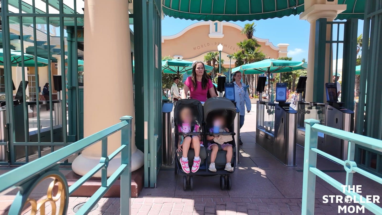 Two children sitting in the Zoe Twin V3 at a theme park entrance, showing seat fit, legroom and different canopy positions.